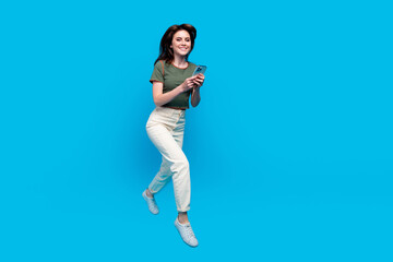 Full size photo of smart lovely woman wear green t-shirt run to empty space with smartphone in hands isolated on blue color background