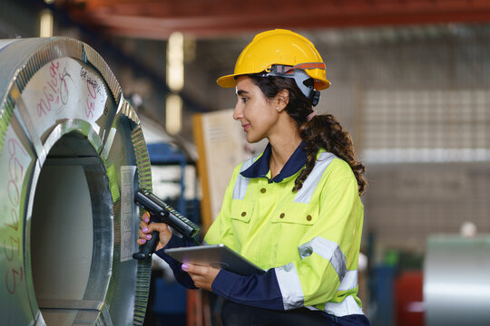 Female Workers in green uniforms and safety helmets perform quality checks inside a metal sheet factory.