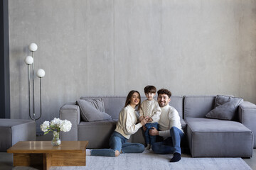 Obraz premium Portrait of happy young Caucasian family with little boy son sit on sofa in new own cozy home.