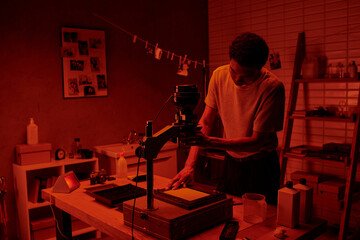 In a red-hued darkroom, a photographer focuses intently on the delicate process of enlarging film