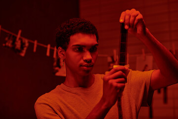 african american photographer examines developed film strip, bathed in darkroom with red light