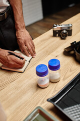cropped african american guy taking notes near bottles with film developing powder in photo lab