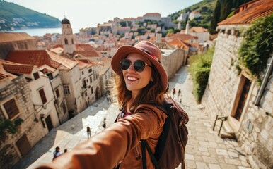 Adriatic Elegance: A Young Native Woman, Backpack-Clad and Radiantly Smiling, Takes a Selfie in Dubrovnik, Croatia, a UNESCO Heritage City, Immersed in Historic Splendor by the Adriatic Sea.