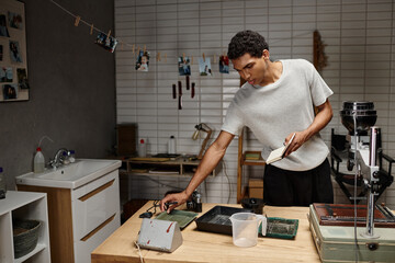 young african american guy holding notebook and standing near analog camera and tools in darkroom
