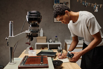 African American photographer immersed in writing while holding analog camera in photo studio