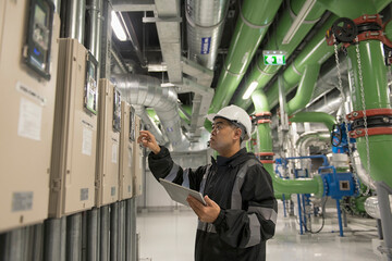 People in Industrial interior chiller and boiler HVAC heating ventilation air conditioning system. person holding a tablet computer on chiller Plant background. Industrial interior chiller.