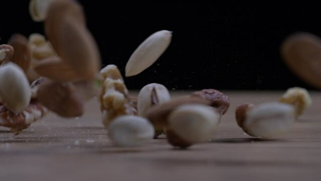 Selection of Nuts Dropping in Slow Motion &ndash; Almonds, Walnuts, Pecans, Cashews, Hazelnuts, and Pistachios Descending onto Wooden Background, macro close-up detail