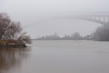 a foggy scene over the Sputin Duyvil Creek off the Hudson River with arch of the Henry Hudson Bridge peeking out of the fog, copy space