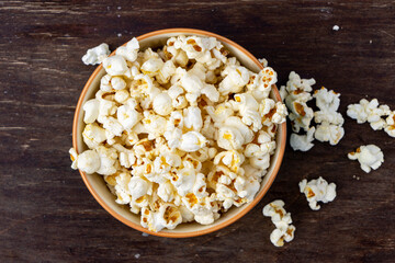 A plate of popcorn on a brown table , top view.
