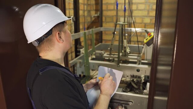 Elevator maintenance. Repair of elevator equipment. Elevator emergency stop. A close-up worker near the elevator car shaft records and measures the elevator's performance readings.