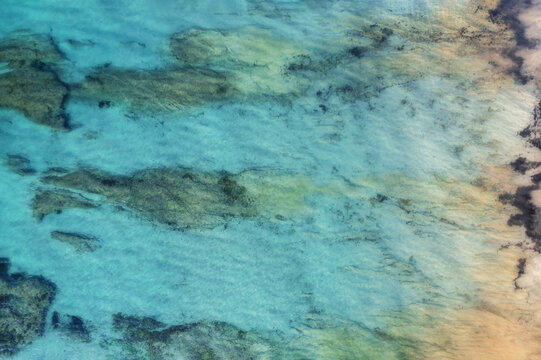 Aerial view of clear blue ocean water with abstract rock formations in the water, creating a pattern, Sellicks Beach, South Australia, Australia.