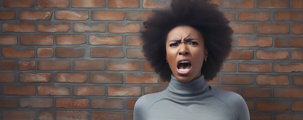 Frustrated African woman in gray sweatshirt against brick wall backdrop expressing anger. Concept Anger, Frustration, Portrait Photography, Brick Wall Background, African Women - obrazy, fototapety, plakaty
