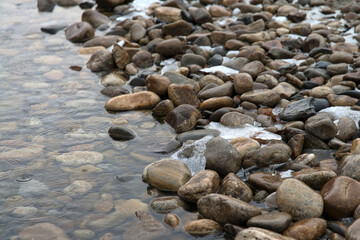 riverside with pebbles, ice, and snow in winter