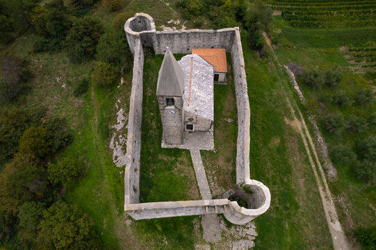 Aerial drone view of Church of the holy trinity (Cerkev Sv. Trojice) surrounded by a wall, Hrastovlje, Koper, Slovenia.