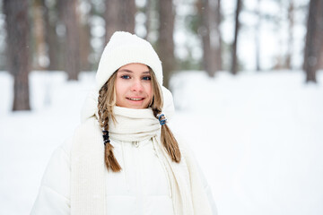 Beautiful Caucasian girl with pigtails in a white coat in winter in the forest, portrait of a young girl