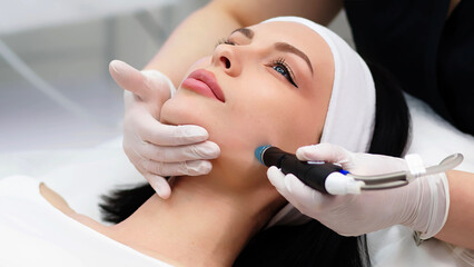 A professional dermatologist wearing medical gloves performs a hydropeeling procedure on a young...