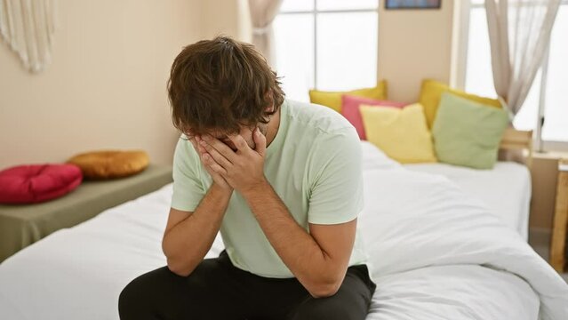 Depression overwhelms young caucasian man in bedroom, crying, face covered. exhausted and worried, his hands hide the sad expression. pyjama-clad, he sobs away his stress indoors.