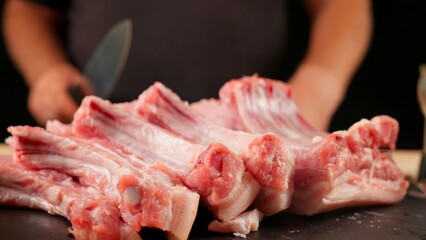 The chef cuts raw meat with a knife. Raw meat-ribs, sliced ​​on a wooden board. Delicious food...