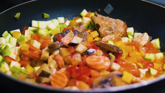Adding frozen vegetables to colorful vegetable stew with meat in a frying pan.