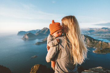 Mother hugging infant baby walking outdoor family lifestyle traveling in Norway summer vacations woman with child in mountains of Lofoten islands aerial view