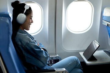 young woman sitting on a plane looking at a tablet for information and entertainment while...