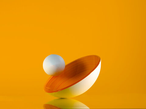 White ball rolling along the rim of a yellow bowl tipped on its side