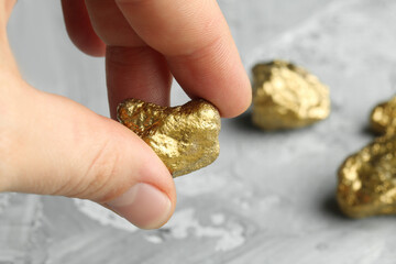 Fototapeta premium Woman holding gold nugget at grey textured table, closeup. Space for text