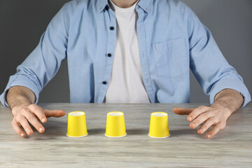 Man playing shell game at wooden table, closeup