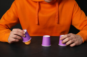 Shell game. Man showing ball under cup at black table, closeup