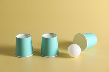 Shell game. Three paper cups and ball on yellow background
