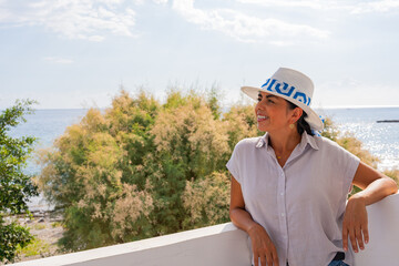 Woman with hat smiling enjoying splendid views of the Aegean Sea from the terrace of her hotel on a...