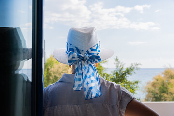 Woman leaning on the glass with a Greek hat enjoying the splendid views from the terrace of her...