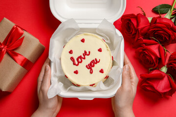 Woman holding takeaway box with bento cake at red table, top view. St. Valentine's day surprise