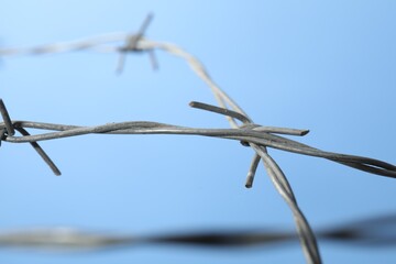 Metal barbed wire on light blue background, closeup