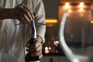Man opening wine bottle with corkscrew on blurred background, closeup