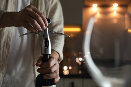 Man opening wine bottle with corkscrew on blurred background, closeup - Powered by Adobe