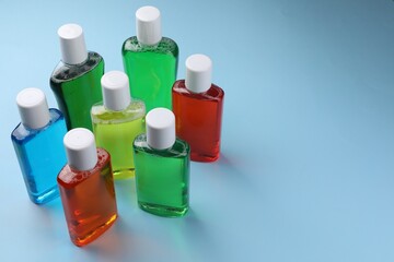 Fresh mouthwashes in bottles on light blue background. Space for text