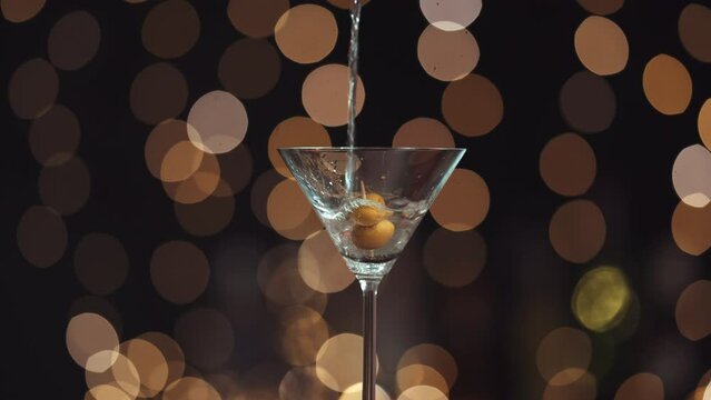 Llena la copa de Martini con alcohol l&iacute;quido, tiene dos aceitunas en un palillo. Todo el fondo est&aacute; desenfocado, creando un efecto bokeh con las luces de fondo. Primer plano del relleno de vidrio.