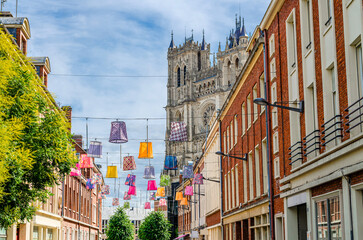 Multicolored chinese lanterns between buildings in old historical city centre, Cathedral Basilica of Our Lady of Amiens Notre-Dame background, Amiens cityscape, Hauts-de-France Region, France - obrazy, fototapety, plakaty
