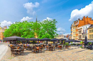 Street restaurant with tables, chairs and umbrellas, green trees and old buildings on Grote Markt...