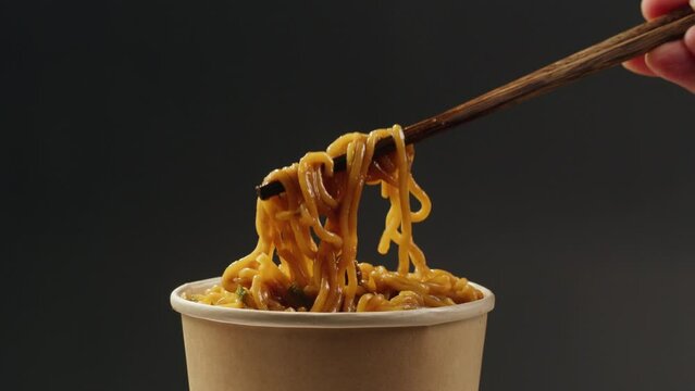Asian fast food noodles with soy meat, parsley close-up. Dropping chopsticks in noodles soup. . Instant noodles, or instant ramen, is a type of food consisting of noodles sold in a precooked and dried