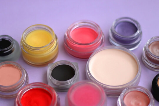 Bowls with various colorful cream beauty products on purple background. Selective focus.