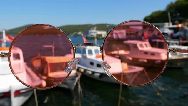 Experience dual perspective through rose-tinted glasses as you gaze upon moored fishing boats along quay of Istanbul's Princes' Islands. This unique POV captures contrasting worlds of tourism