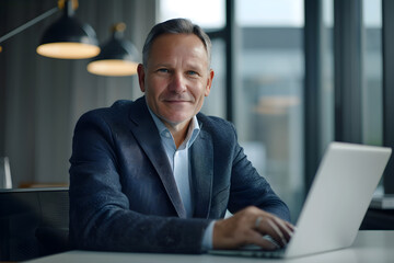 businessman working on laptop in the office. business attire. smiling, senior or middle aged. suit and shirt. bright day
