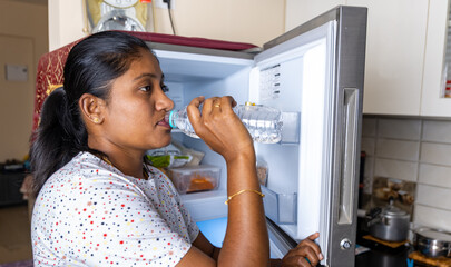 indian woman drinking water from a bottle in the kitchen at home