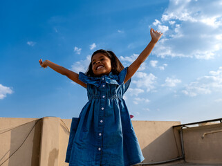 A Cute Indian little girl jumping in the air with blue sky background