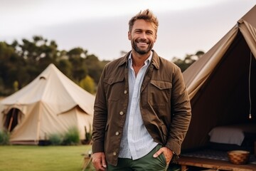 Portrait of smiling man standing with hands in pockets at campsite