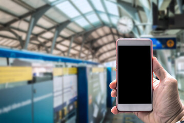 Close-up of a hand holding a blank-screen smartphone with a blurred train station background,...