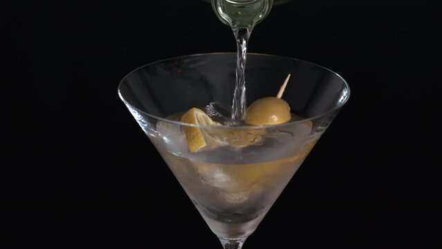 detalle de primer plano llene la copa de Martini con alcohol l&iacute;quido, tiene una rodaja de lim&oacute;n y hielo y dos aceitunas en un palillo. Se puede ver la boquilla de la botella por donde sale el l&iacute;quido.