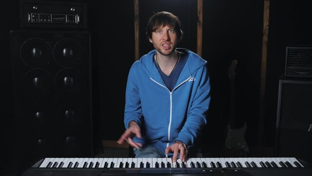 Footage of a pianist giving a lesson or master class, looking into the camera, offering detailed descriptions of chords and techniques to his audience, sitting at music studio. Online piano courses. 